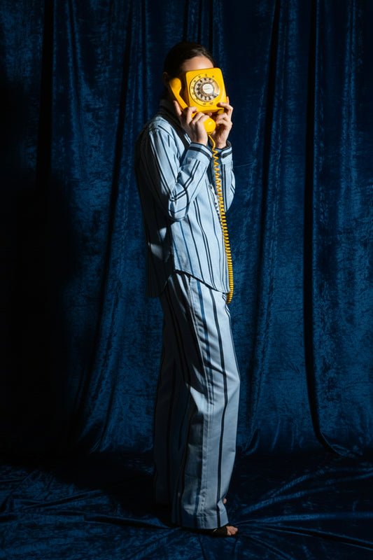 Person holding a yellow rotary phone against a dark blue curtain