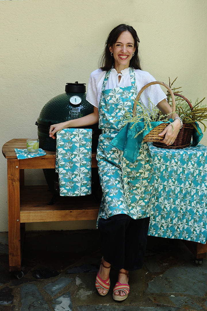 Woman in a kitchen setting with a large green grill, table, and floral apron.